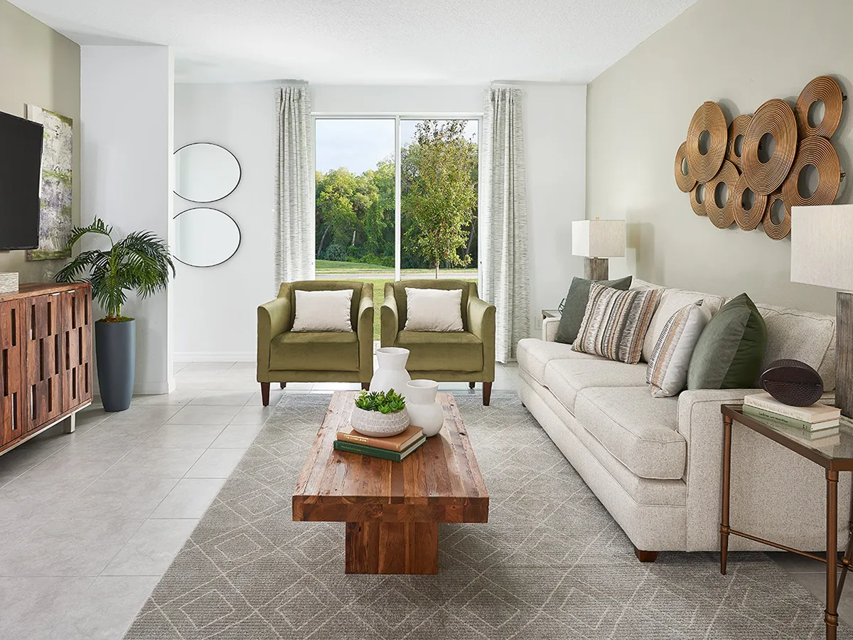 Modern living room with a beige sofa, two green armchairs, wooden coffee table, decorative wall art, plants, and large window with sheer curtains letting in natural light. Neutral tones and geometric rug create a cozy, inviting space.