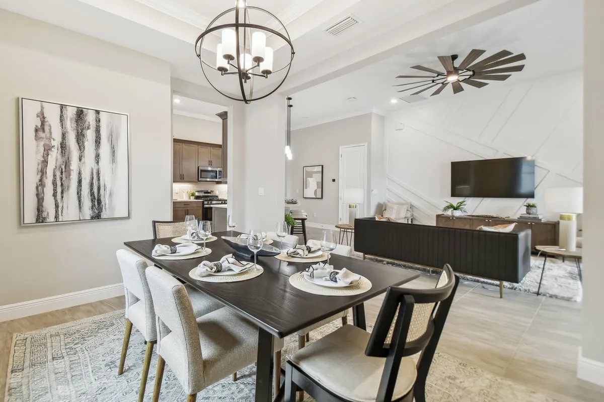 Modern open-concept dining and living area with a dark wood dining table set for six, beige chairs, abstract wall art, neutral decor, a chandelier, and a distant view of the kitchen and living room with TV.