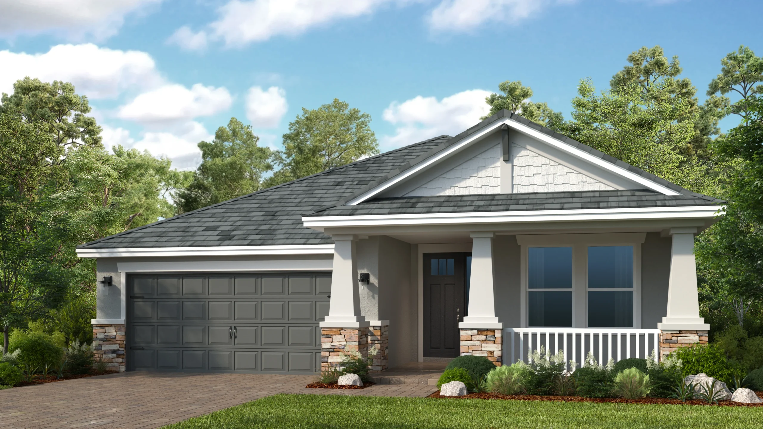A single-story suburban house with a gray shingled roof, a double garage, stone accents on the columns, a small front porch with white railing, and neatly landscaped greenery in front.