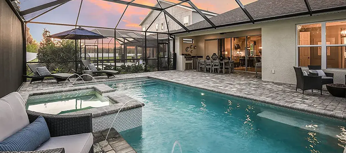 A screened-in backyard patio features a swimming pool with a spa, outdoor seating, and dining area. The sky is colorful at sunset, and the house’s windows reveal a warmly lit interior.