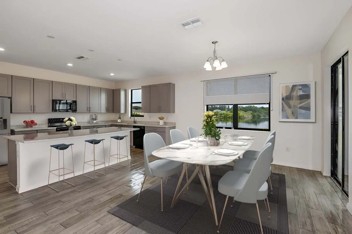 Modern kitchen and dining area with light gray cabinets, a large marble dining table set for six, barstools at the kitchen island, wood flooring, and large windows with a view of a lake.