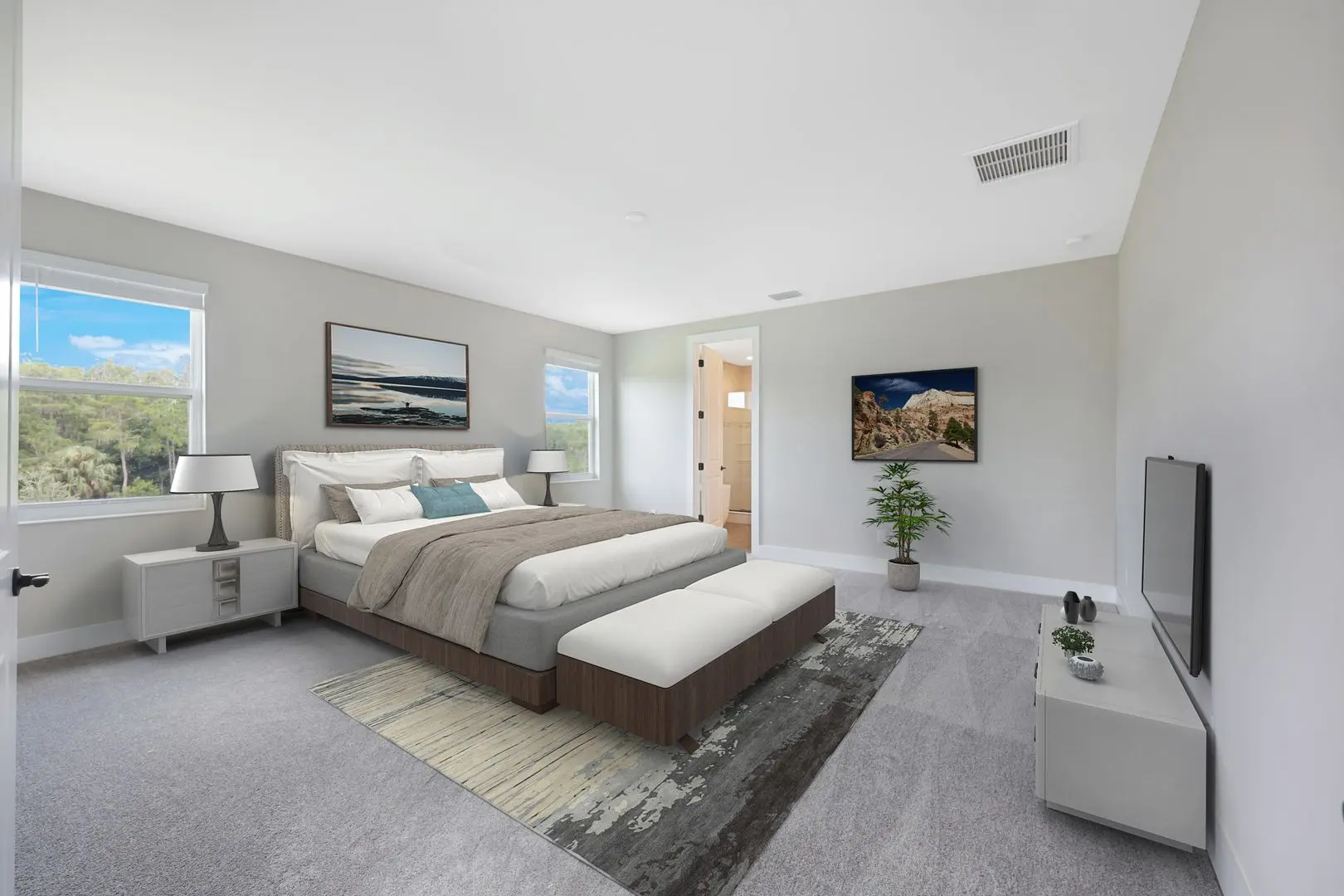 Modern bedroom with a large bed, white bedding, and a padded bench at the foot. There are nightstands, lamps, landscape artwork, a TV on a low stand, a rug, and large windows with a scenic outdoor view.