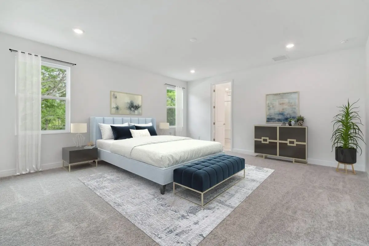 Modern, spacious bedroom with a light gray upholstered bed, blue bench, two nightstands with lamps, a large area rug, dresser, two abstract paintings, a potted plant, and windows with white curtains letting in natural light.
