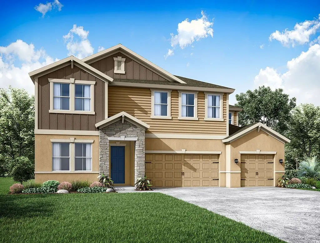 A modern two-story house with tan and brown siding, stone accents around the front door, multiple windows, and a three-car garage. The home is surrounded by green grass and landscaping under a blue sky with clouds.