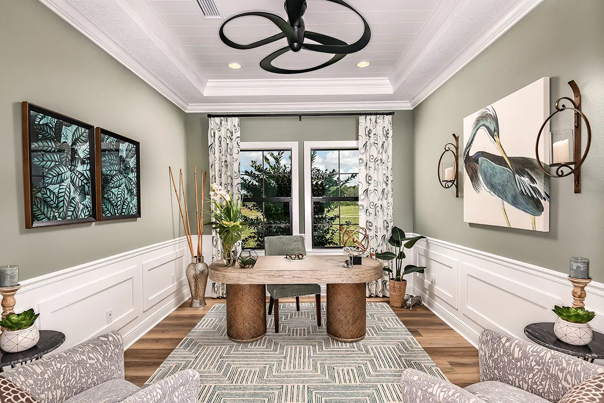 A bright, modern home office with a large wooden desk, patterned rug, two armchairs, wall art, plants, and windows with curtains overlooking greenery outside. Contemporary decor and neutral tones create a cozy atmosphere.