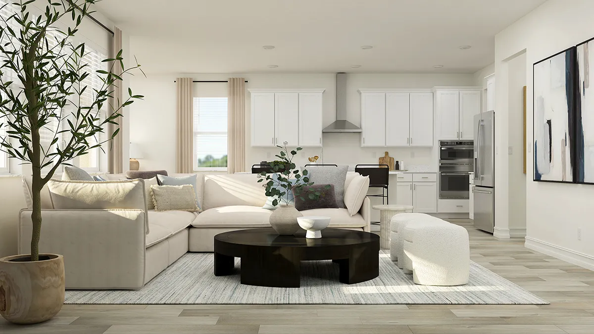 Modern living room with a beige sectional sofa, round black coffee table, textured ottoman, potted plant, large abstract wall art, and an open kitchen with white cabinets and stainless steel appliances in the background.