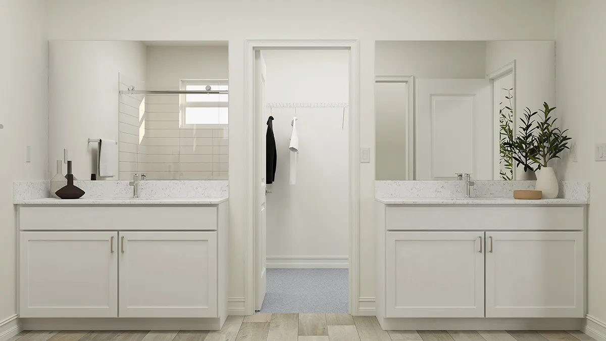 Modern bathroom with two white vanities and large mirrors on either side of a central doorway leading to a walk-in closet. Each vanity has a sink and decorative items; a plant decorates the right side.