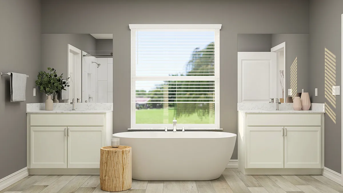 Modern bathroom with a freestanding white bathtub centered beneath a large window with blinds, flanked by two vanities with sinks, mirrors, and decorative items, plus a wooden stool on a light wood floor.