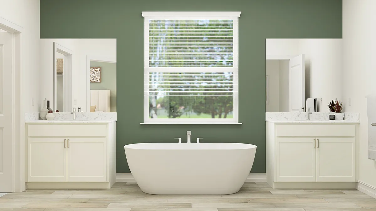 Modern bathroom with a freestanding white bathtub centered under a window with blinds, flanked by two white vanities with marble countertops, against a green accent wall and light wood flooring.